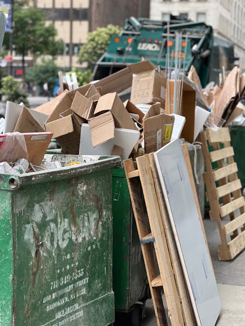 A person’s hand is shown placing a crumpled paper bag into a white rubbish bin with a partially open lid, situated on a surface with a wooden texture. The paper bag appears brown and slightly crease